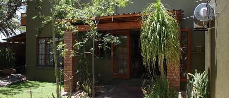 Una casa moderna con fachada de ladrillo, una pérgola de madera y diversas plantas.