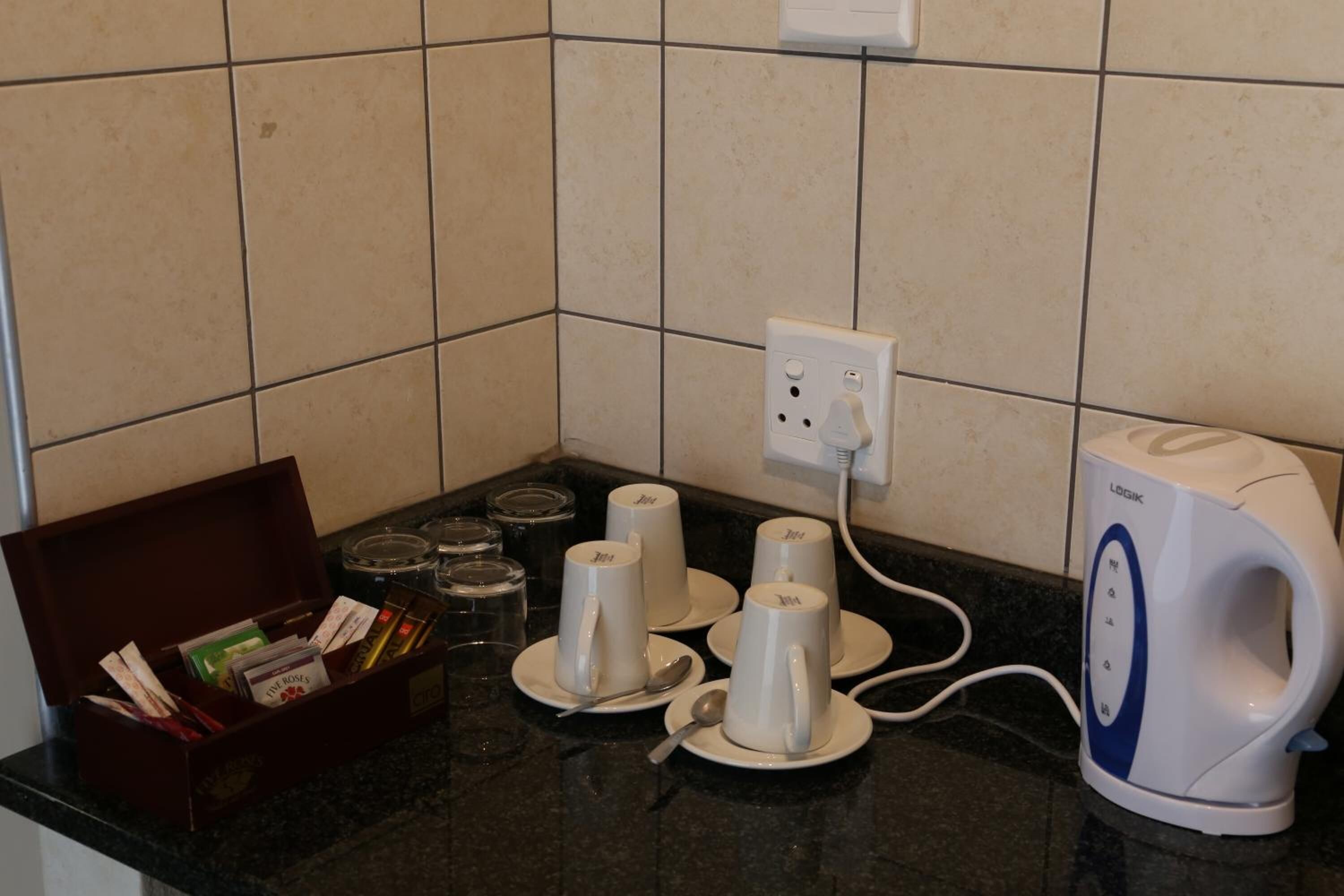 A kitchen counter with a coffee maker, a box of tea bags, and several cups.