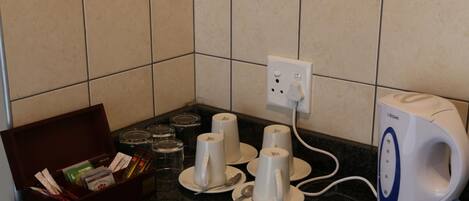 A kitchen counter with a coffee maker, a box of tea bags, and several cups.