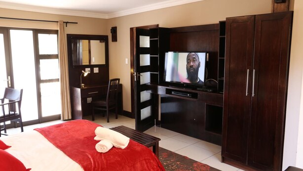 A hotel room with a bed, a desk, a television, and a wardrobe. - Klein Windhoek Guesthouse (Windhoek)