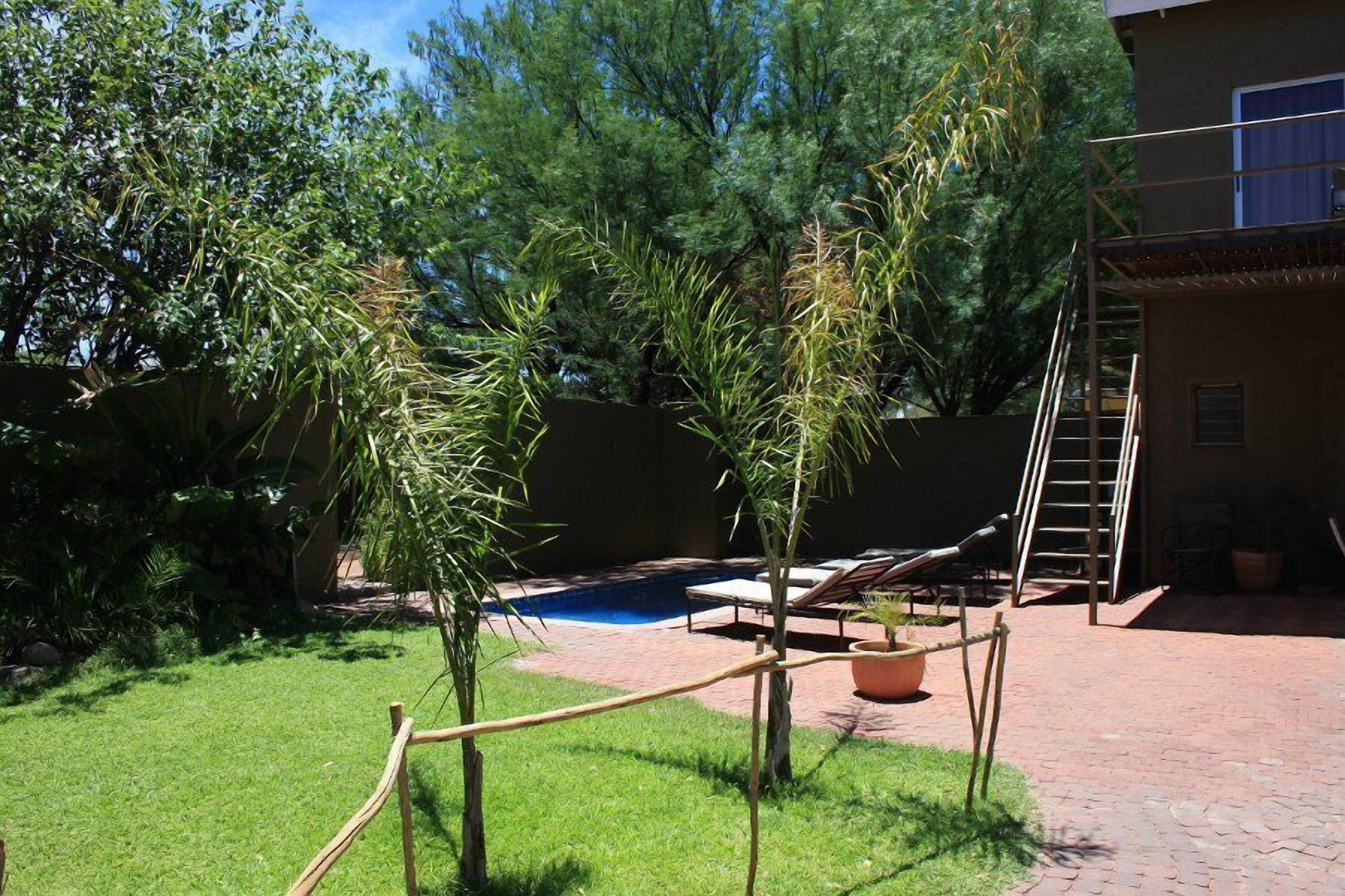 A backyard with a swimming pool, a wooden deck, and a ladder leading to a building.