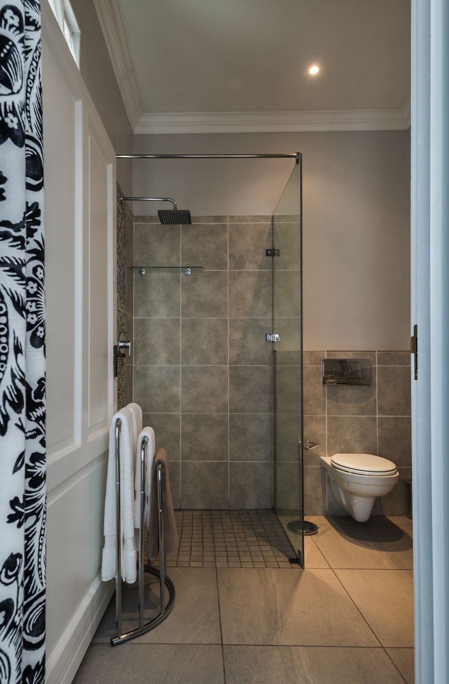 A modern bathroom with a glass shower enclosure, a toilet, and a towel rack.