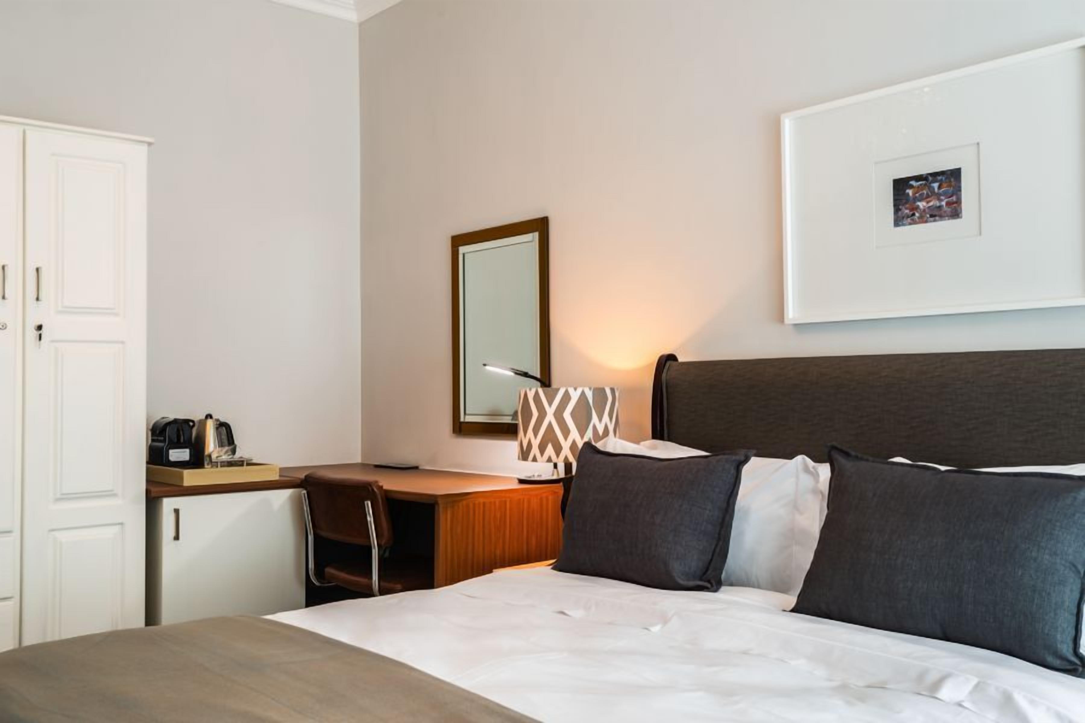 Una habitación de hotel con cama, escritorio, silla, lámpara y un cuadro en la pared.