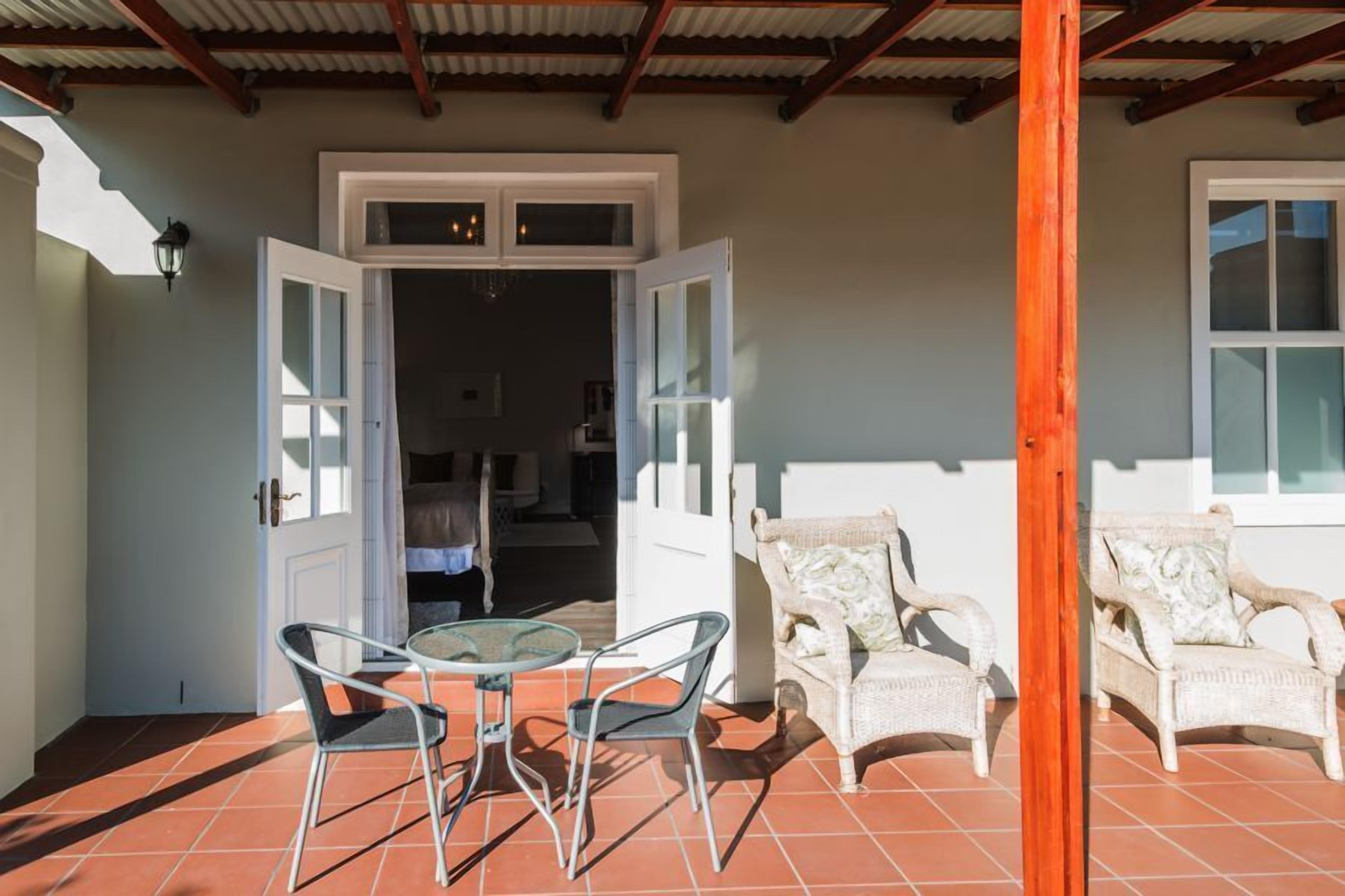 Un patio cubierto con una mesa y sillas, un poste de madera y vistas a una habitación con cama y ventana.