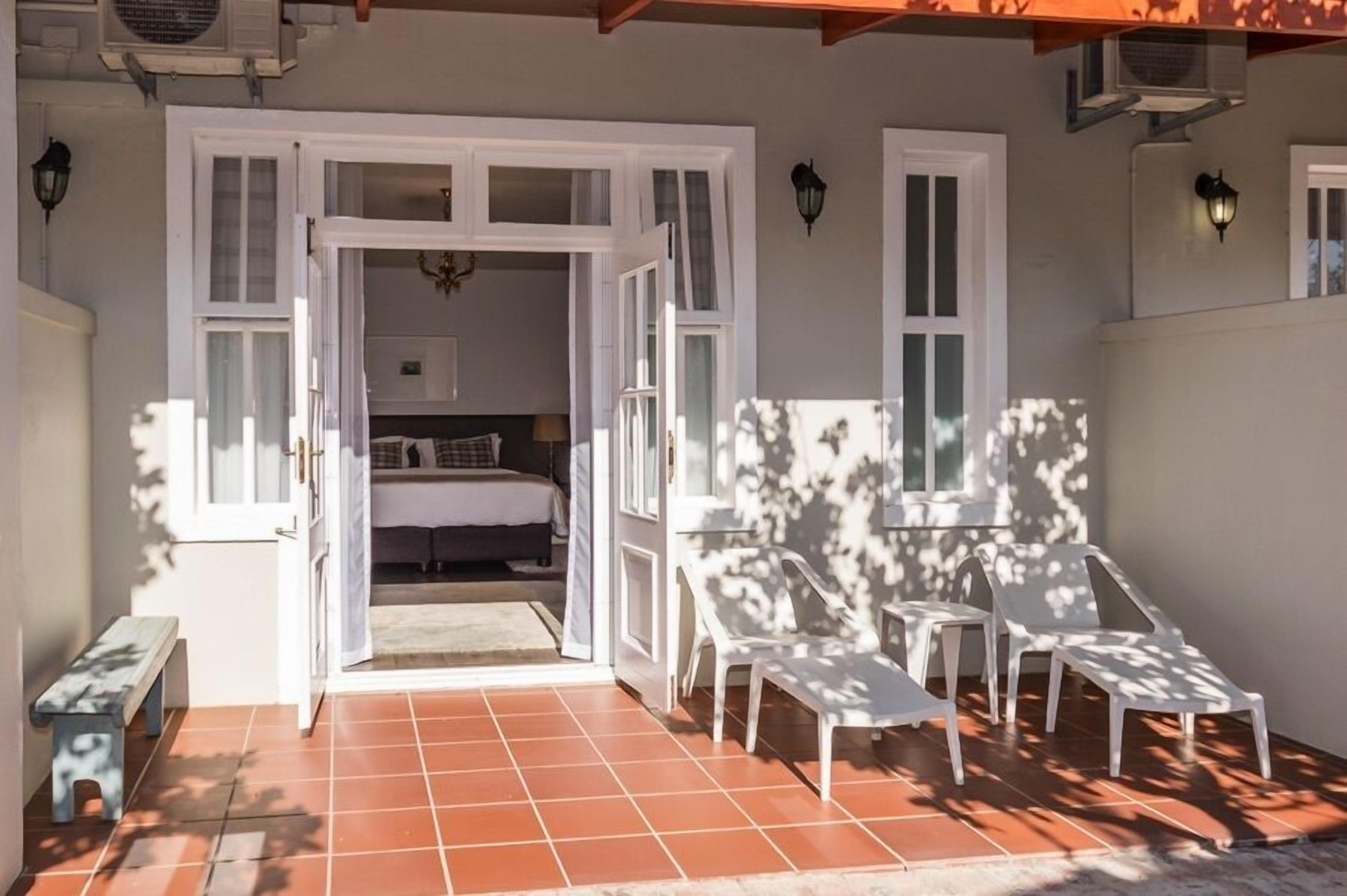 An open doorway leading to a bedroom with a bed and a chandelier. There are white chairs and a bench outside the room.