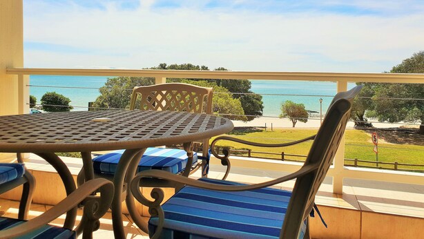 A balcony with a table and chairs, overlooking a beach and the sea. - Gold Water (Cape Town)