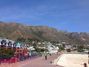 A coastal promenade with a blue and red fence, a beach, and houses in the background. - Bergsig Self-Catering (Cape Town)