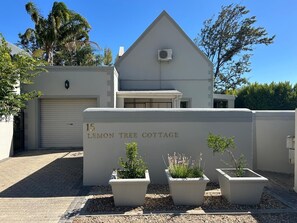 A modern building with a grey facade, a garage door, and three potted plants in front. - Lemon Tree Cottage (Franschhoek)