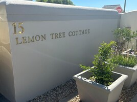 Un bâtiment sur lequel on peut lire l’inscription « 15 LEMON TREE COTTAGE », avec des plantes en pot devant l’entrée.