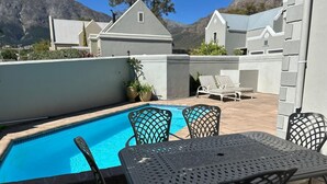 A pool area with a table and chairs, surrounded by a low wall and potted plants. - Lemon Tree Cottage (Franschhoek)