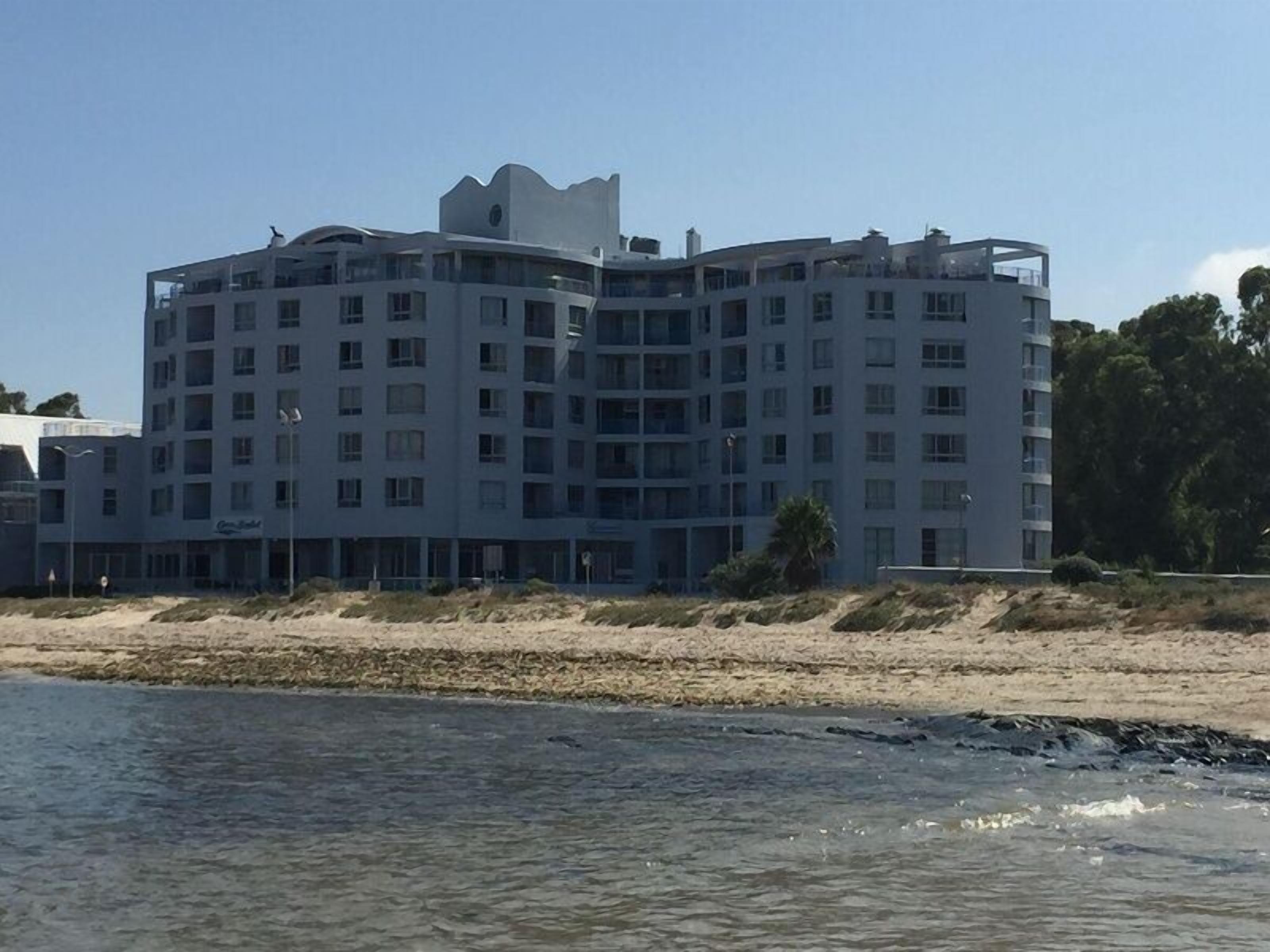 A multi-story hotel with a modern architectural design, featuring balconies and a beachfront location.
