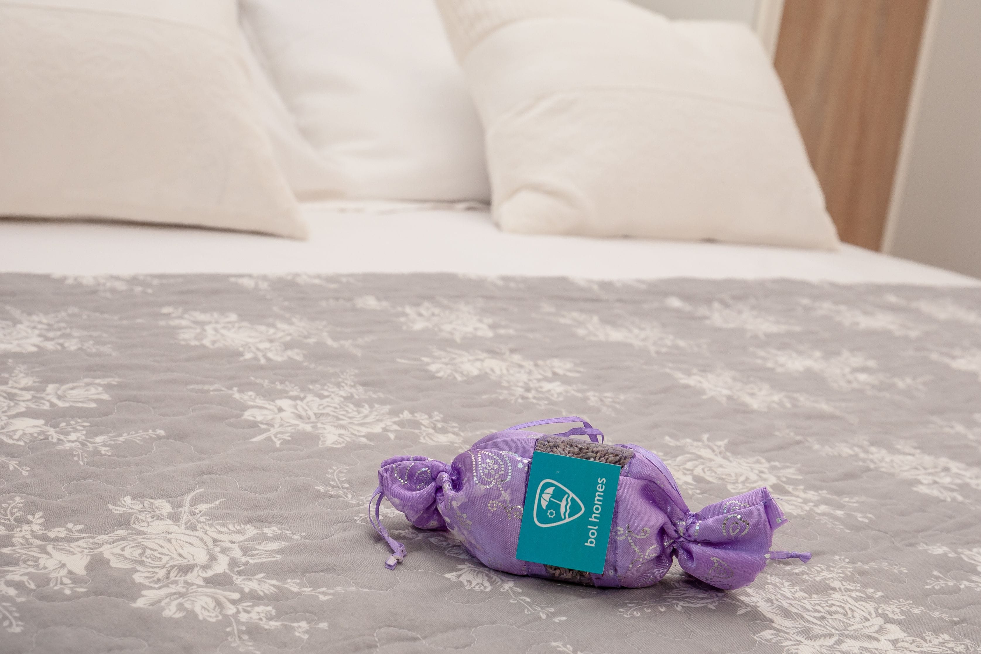 Een bed met een bloemenprintdeken en een paars cadeauzakje met een blauwgroene tag.