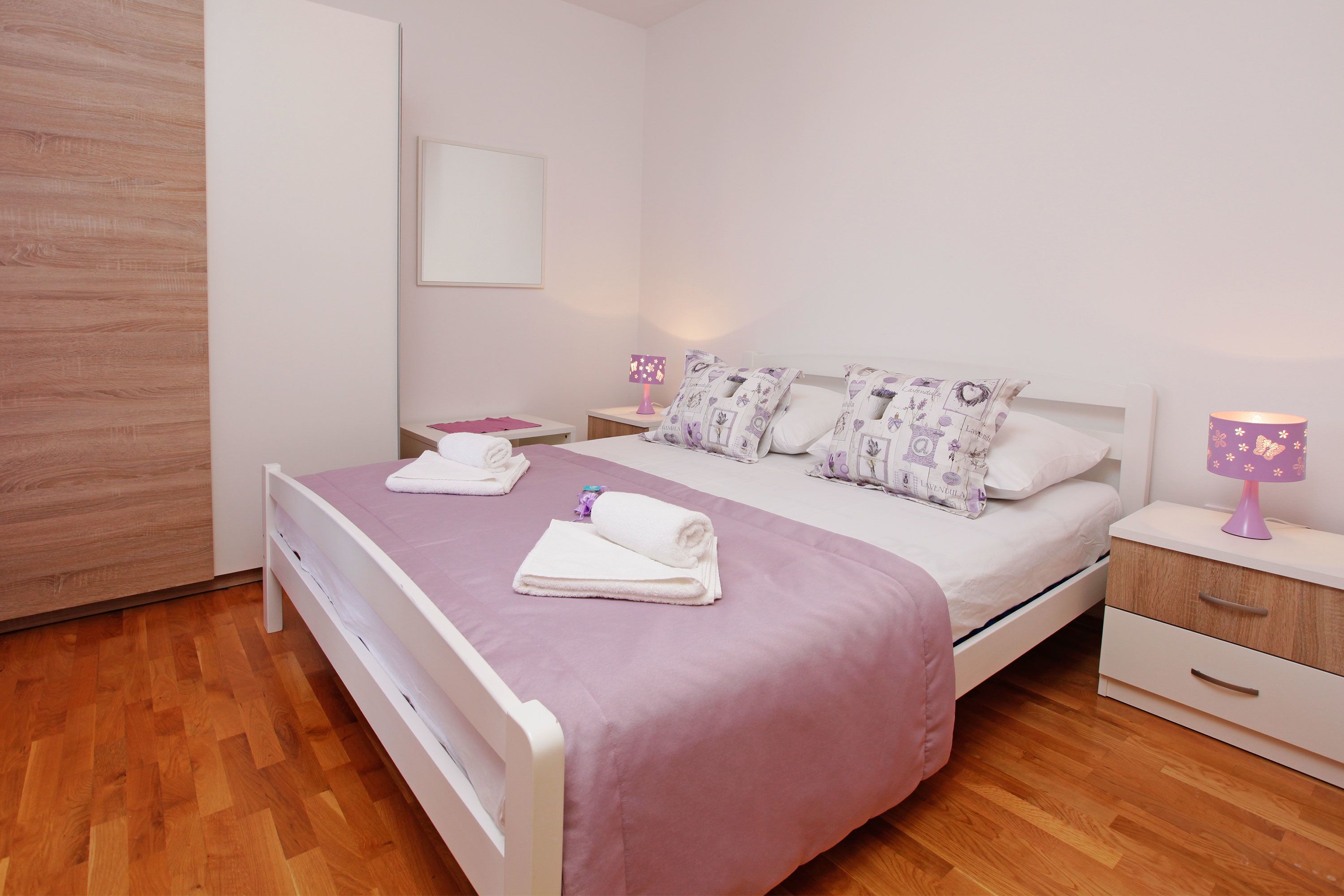 A neatly made bed with a pink bedspread, two white pillows, and a bedside table with a lamp.