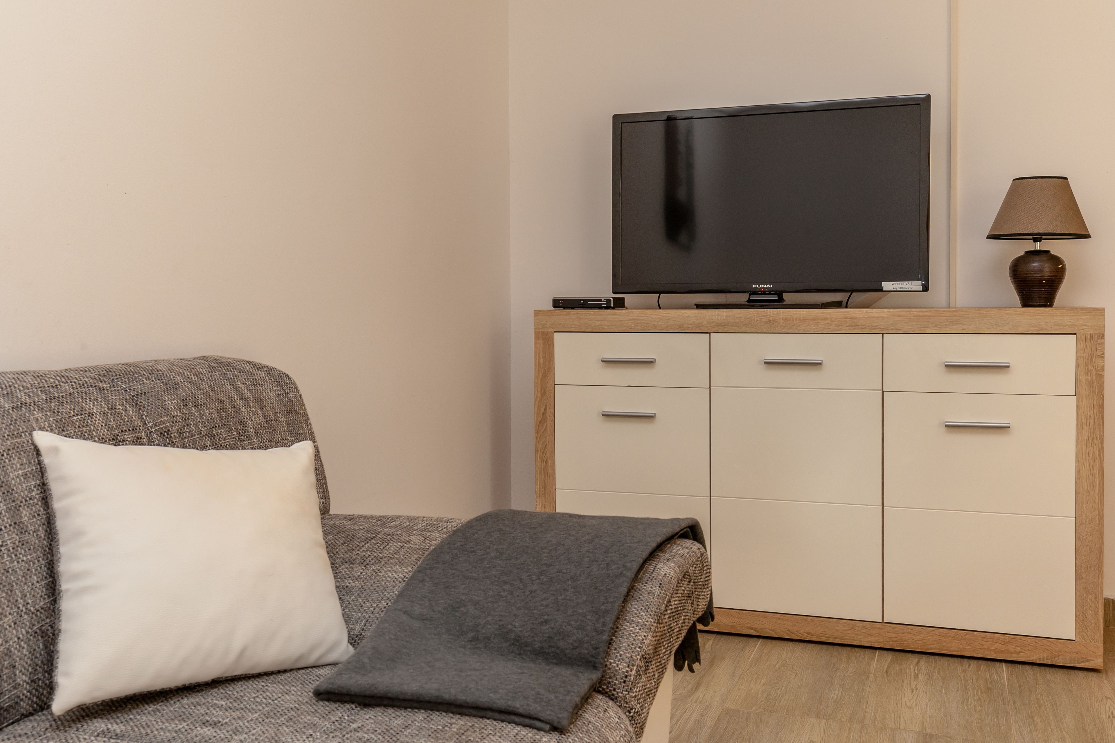 Una sala de estar con un sofá, un televisor sobre un mueble de madera y una lámpara.