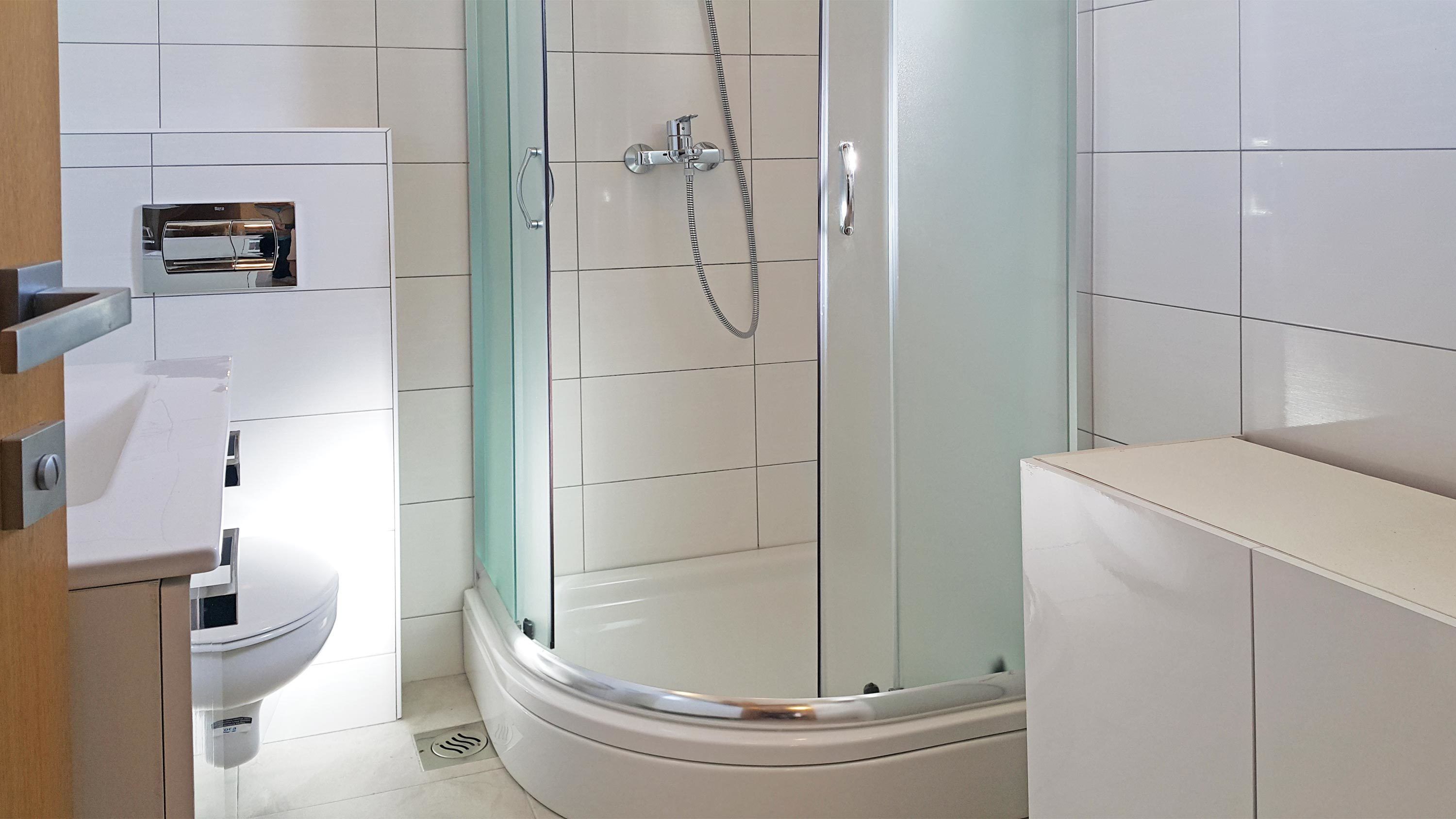 A modern bathroom with a glass-enclosed shower, white tiles, and a toilet.