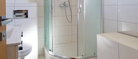 A modern bathroom with a glass-enclosed shower, white tiles, and a toilet.