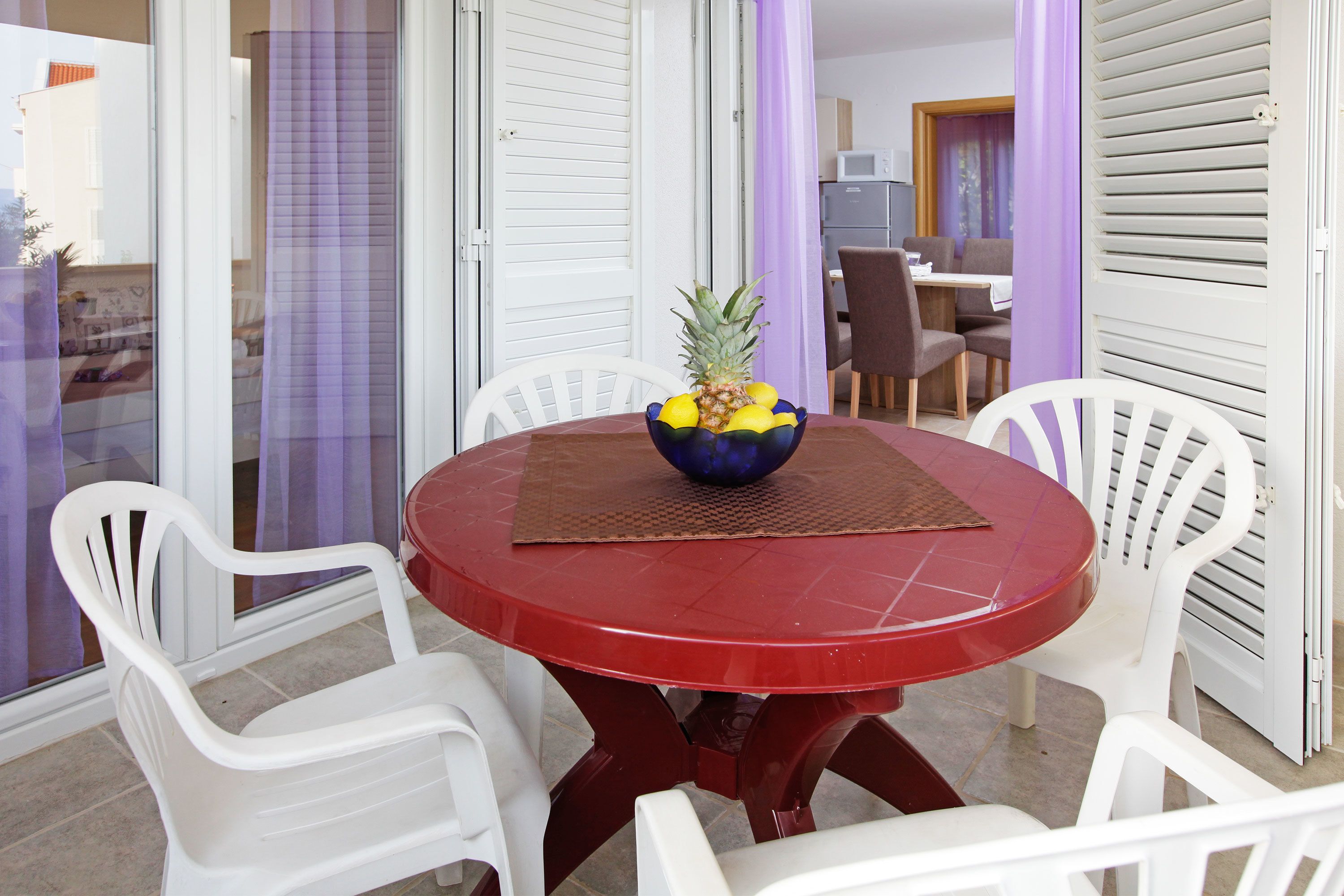 A dining area with a red table, white chairs, and a bowl of fruit on the table.