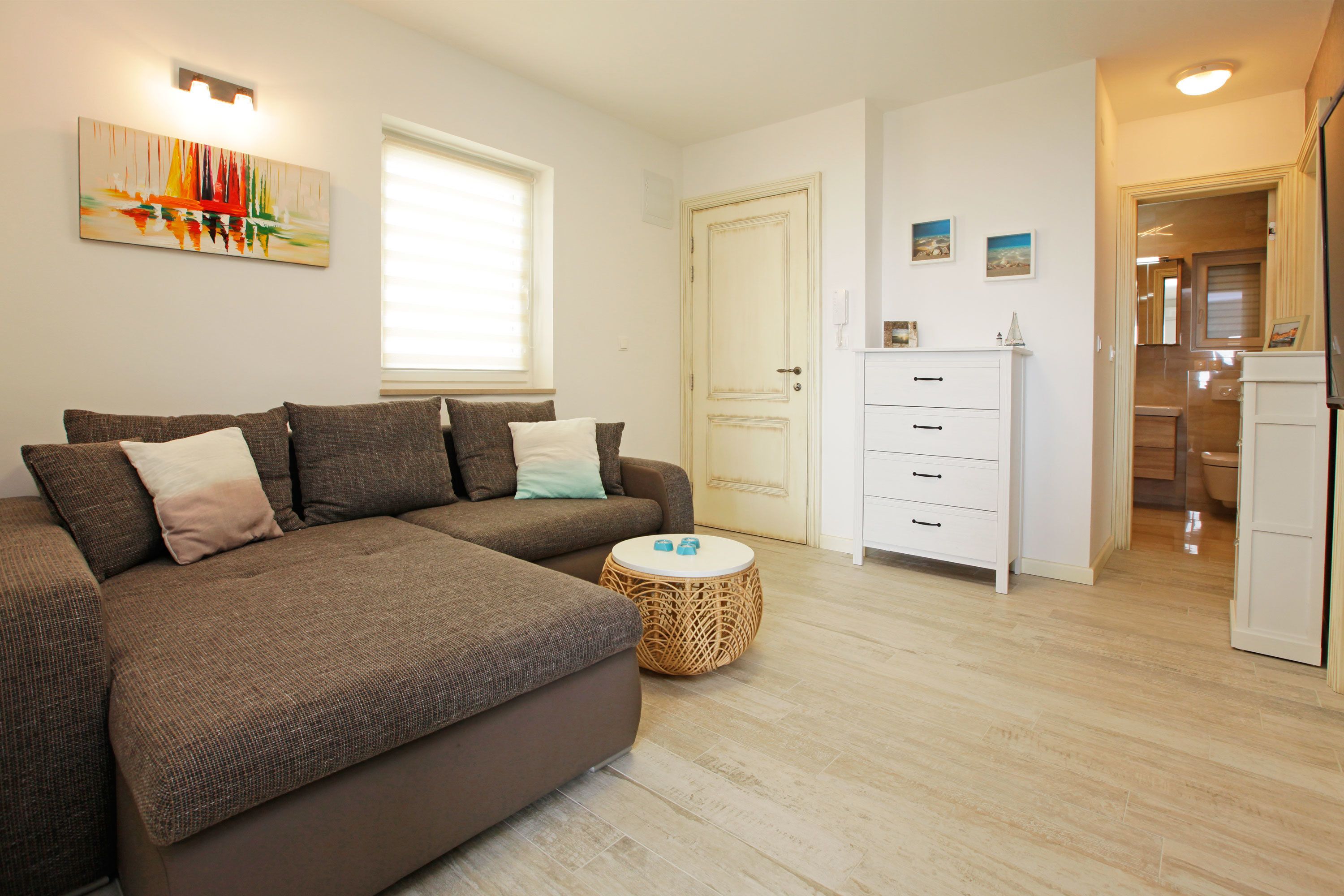 A modern living room with a brown sectional sofa, a round wicker side table, and a white cabinet.
