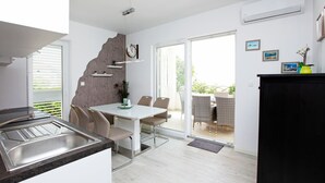 Una cocina moderna con pileta integrada, un comedor con mesa y sillas blancas, y un balcón con mobiliario de mimbre.