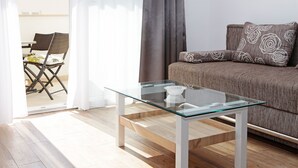 Una sala de estar moderna con una mesa de centro de vidrio, un sofá con cojines estampados y una zona de comedor con una silla y una mesa.