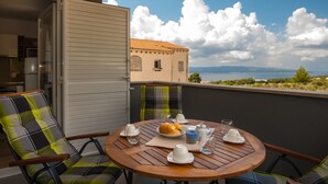Un balcón con una mesa de madera dispuesta para el desayuno, con cruasanes y tazas, que ofrece una vista panorámica de un edificio y montañas.