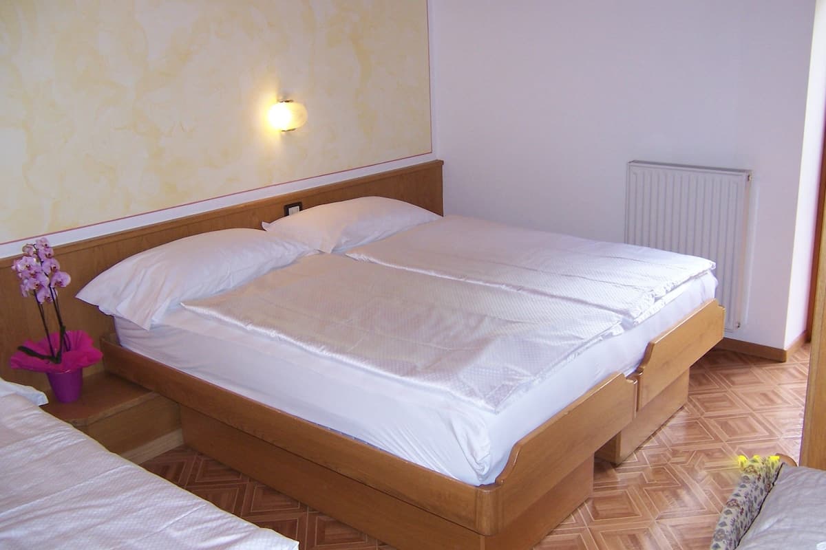 A bedroom with a wooden bed, white bedding, a wall-mounted light, and a radiator.