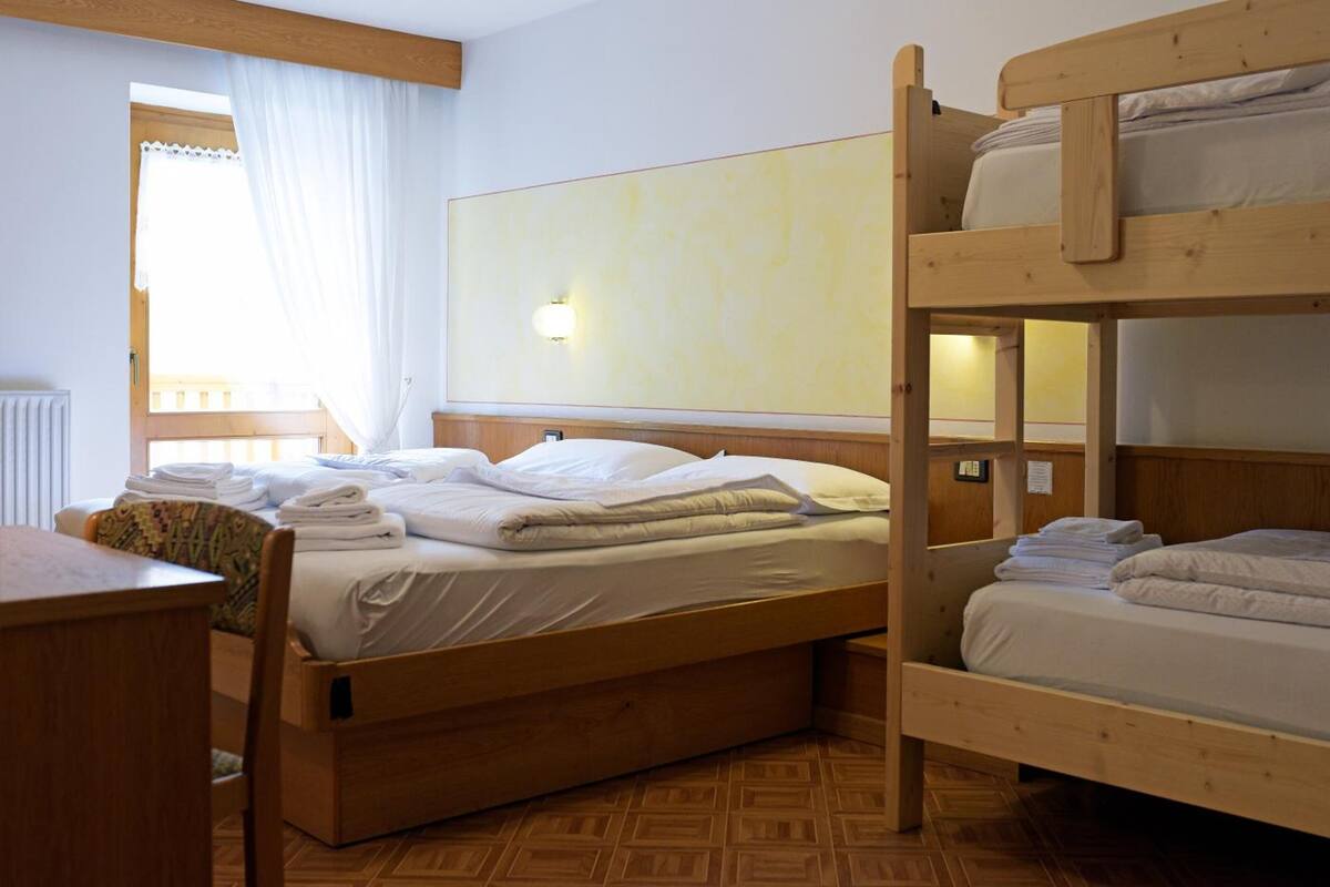 A room with two bunk beds, a wooden dresser, a radiator, and a window with curtains.