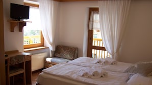 A bedroom with a bed, a desk, a chair, a television, and a window with curtains.
