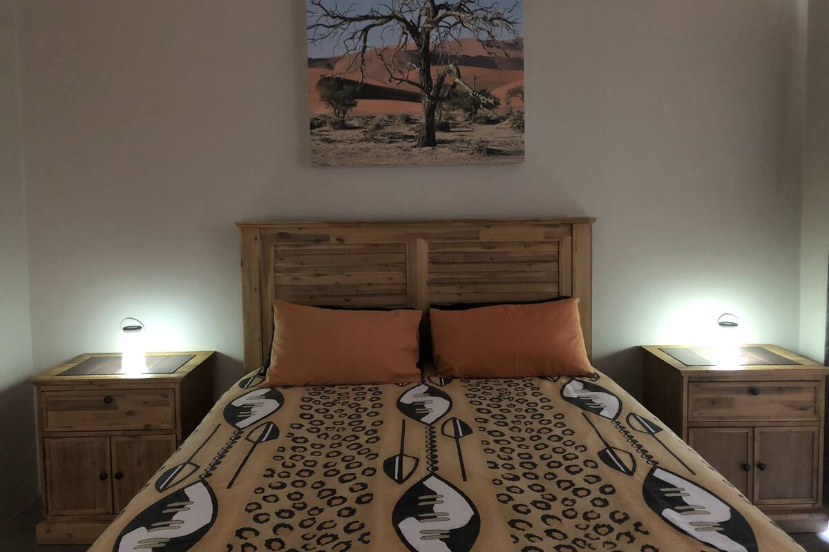 Ein Schlafzimmer mit einem Holz-Kopfteil, zwei Nachttischen, einem Bett mit einem gemusterten Überwurf und einem Gemälde einer Wüstenlandschaft an der Wand.