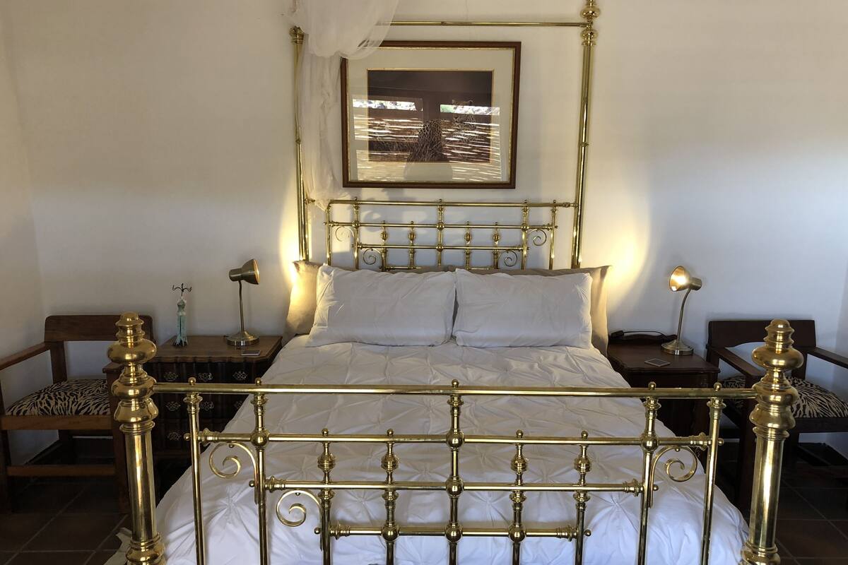 Ein Bett mit Baldachin, dessen goldener Rahmen weiße Bettwäsche und ein gerahmtes Bild darüber ergänzt.
