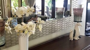 Una stanza con un grande specchio che riflette la vista dalla finestra, un vaso bianco con fiori bianchi e una statuetta di un pinguino decorativo su un tavolo.