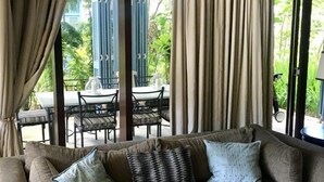 Un soggiorno con divano, tende e vista su una zona pranzo all'aperto.
