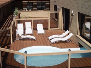 Een houten terras met een jacuzzi, lounge stoelen en een kleine tafel met planten.