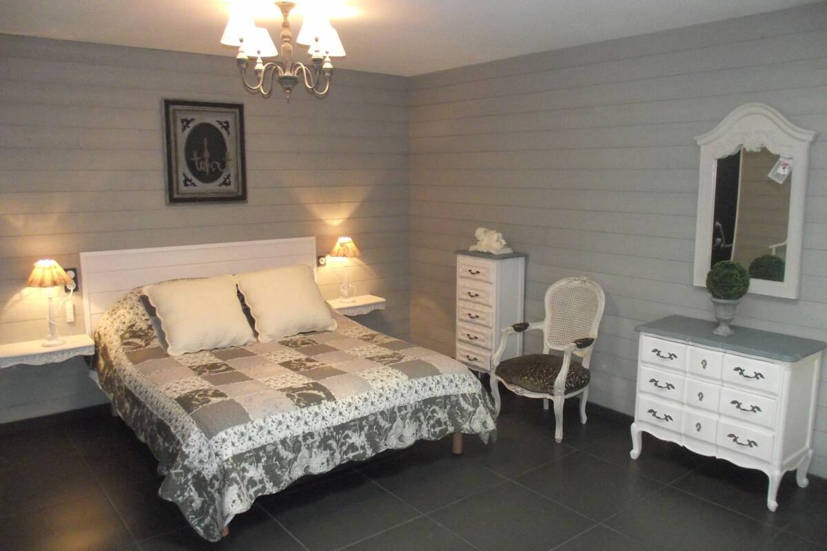 Une chambre à coucher comprenant un lit, des tables de chevet, une commode, une chaise et un miroir.