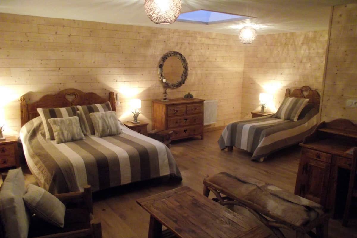 Une chambre confortable avec un grand lit, deux petits lits, des meubles en bois et une lucarne.