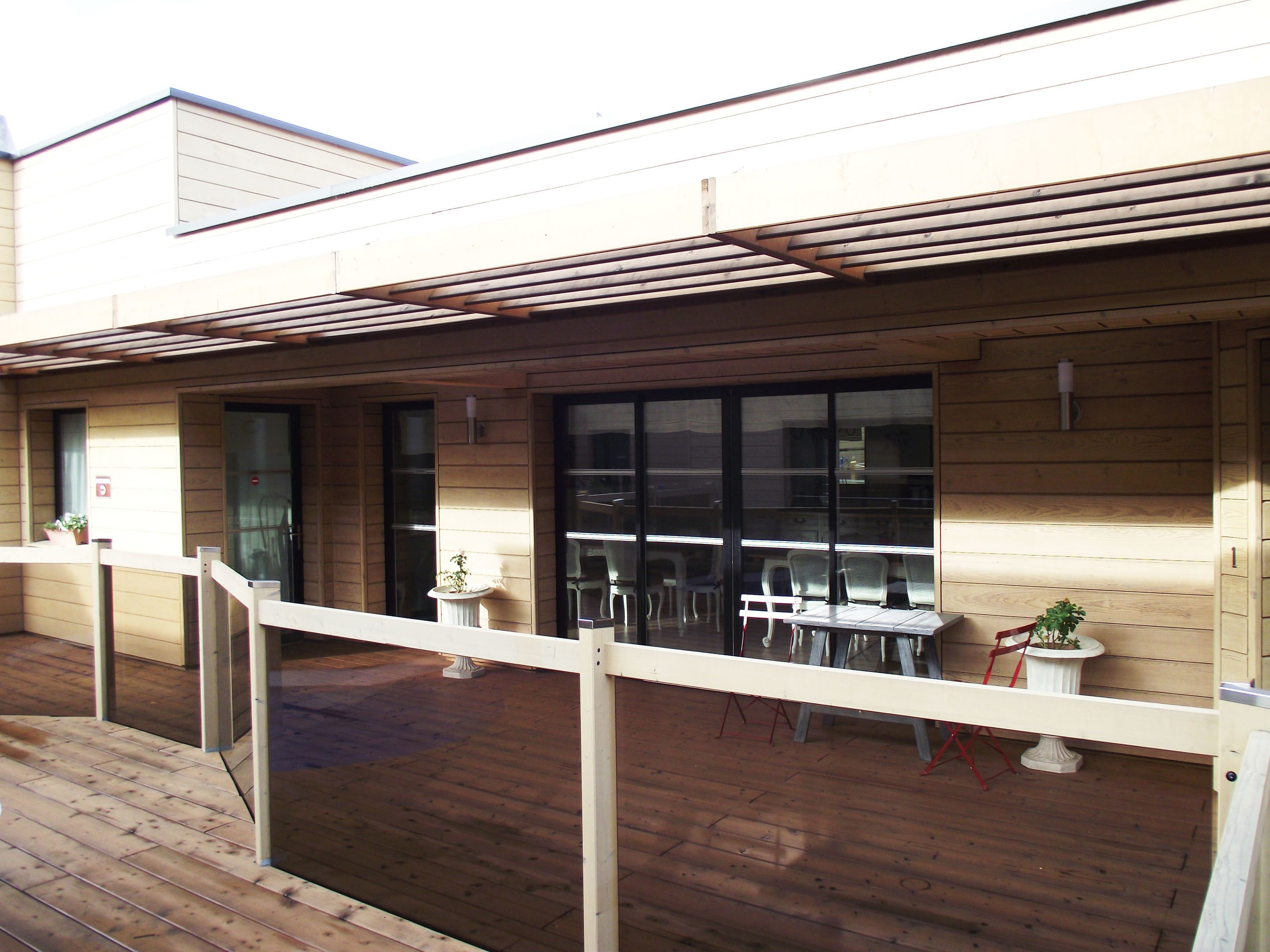 A wooden deck with a covered seating area, a small table, and potted plants.