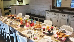 Ein Essbereich mit einem langen Tisch, gedeckt für eine Mahlzeit, umgeben von weißen Stühlen, und eine Küche im Hintergrund.