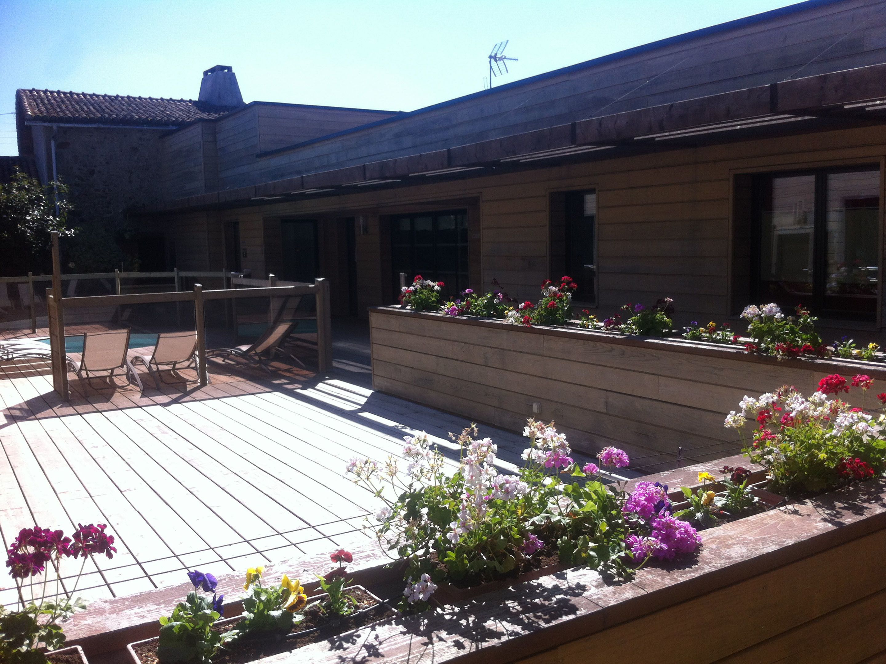 Una terraza de madera con mobiliario exterior y macizos de flores.