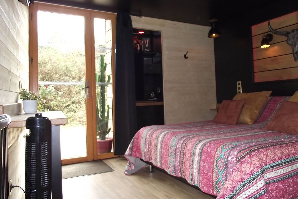 Une chambre à coucher comprenant un lit, un radiateur, une plante en pot et une porte-fenêtre coulissante donnant sur une terrasse.