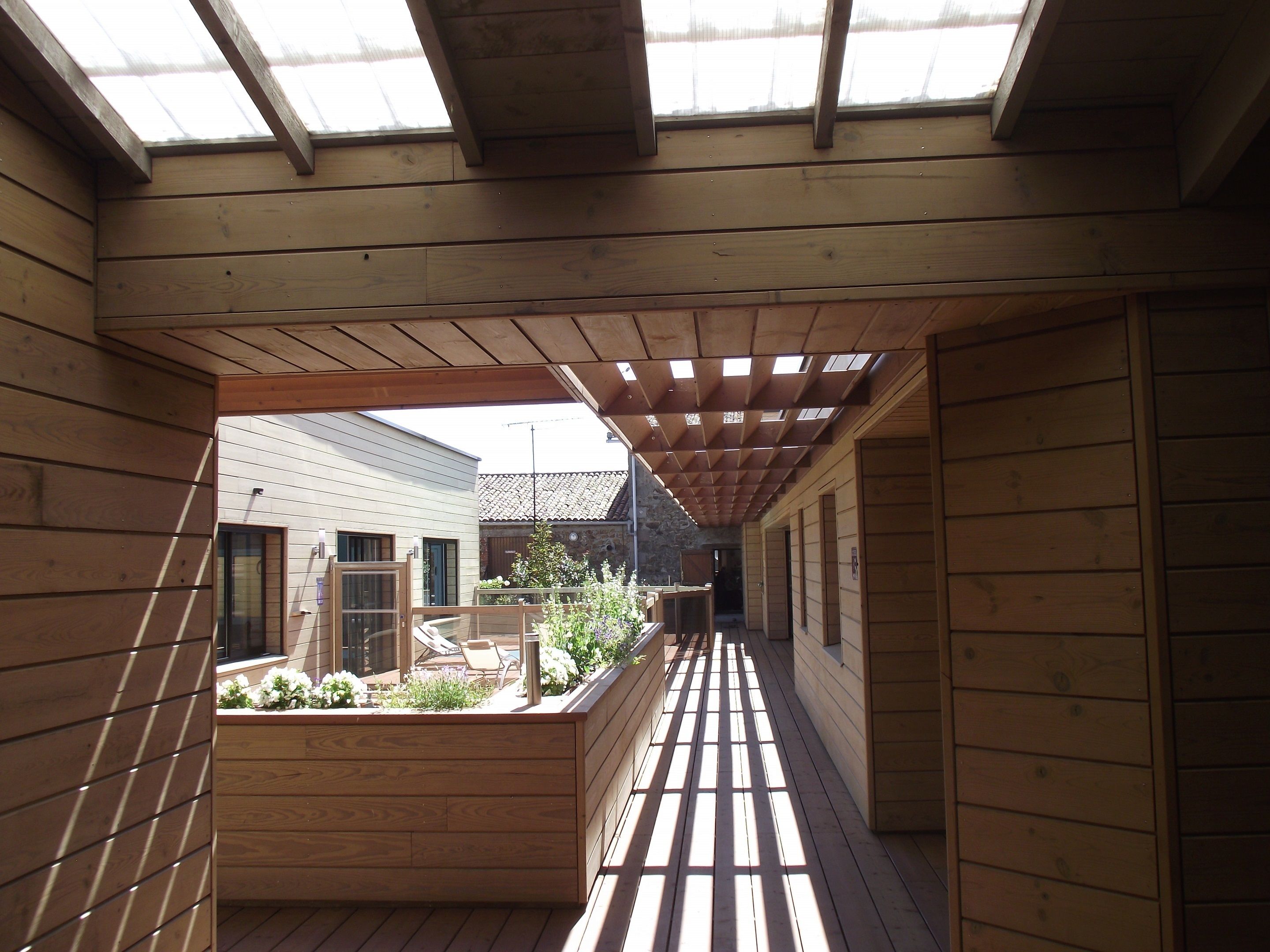 Eine Holzterrasse mit Oberlicht, die in einen Gartenbereich mit Sitzgelegenheit führt.