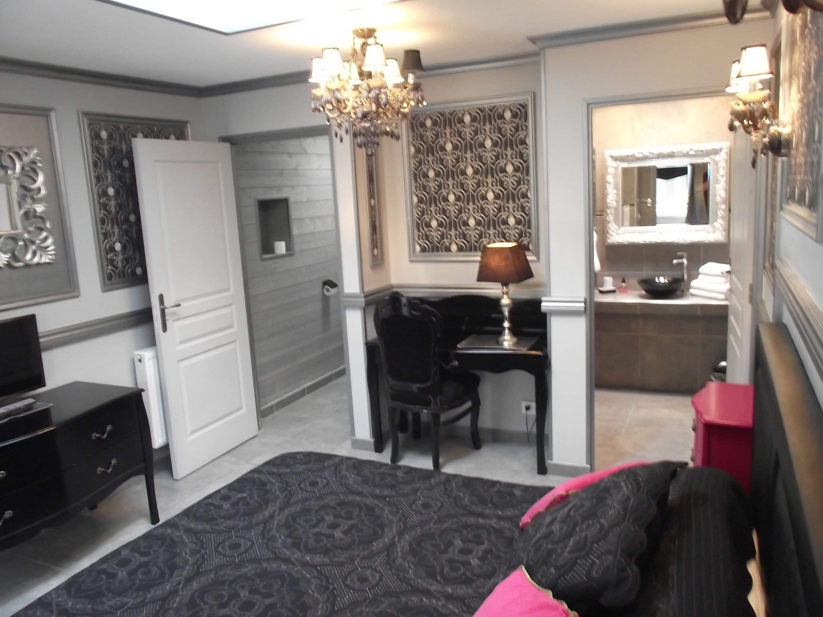 A bedroom with a bed, a desk, a chair, a dresser, a mirror, and a chandelier.