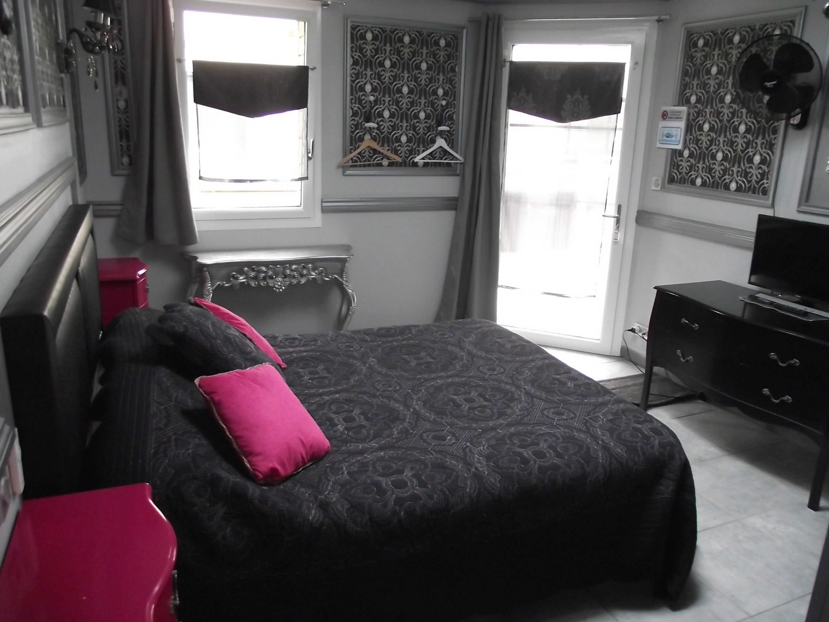 Ein Schlafzimmer mit Bett, Kommode, Fernseher und einem Fenster mit Vorhängen.