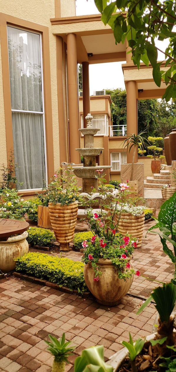 Un patio con una fuente, plantas en macetas y mobiliario de exterior.
