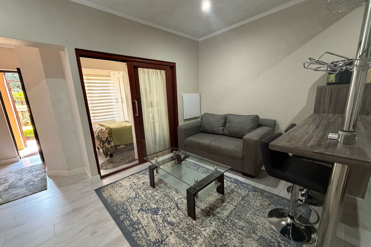 Un salon moderne avec une table basse en verre, un canapé gris et un coin repas avec une chaise en métal.