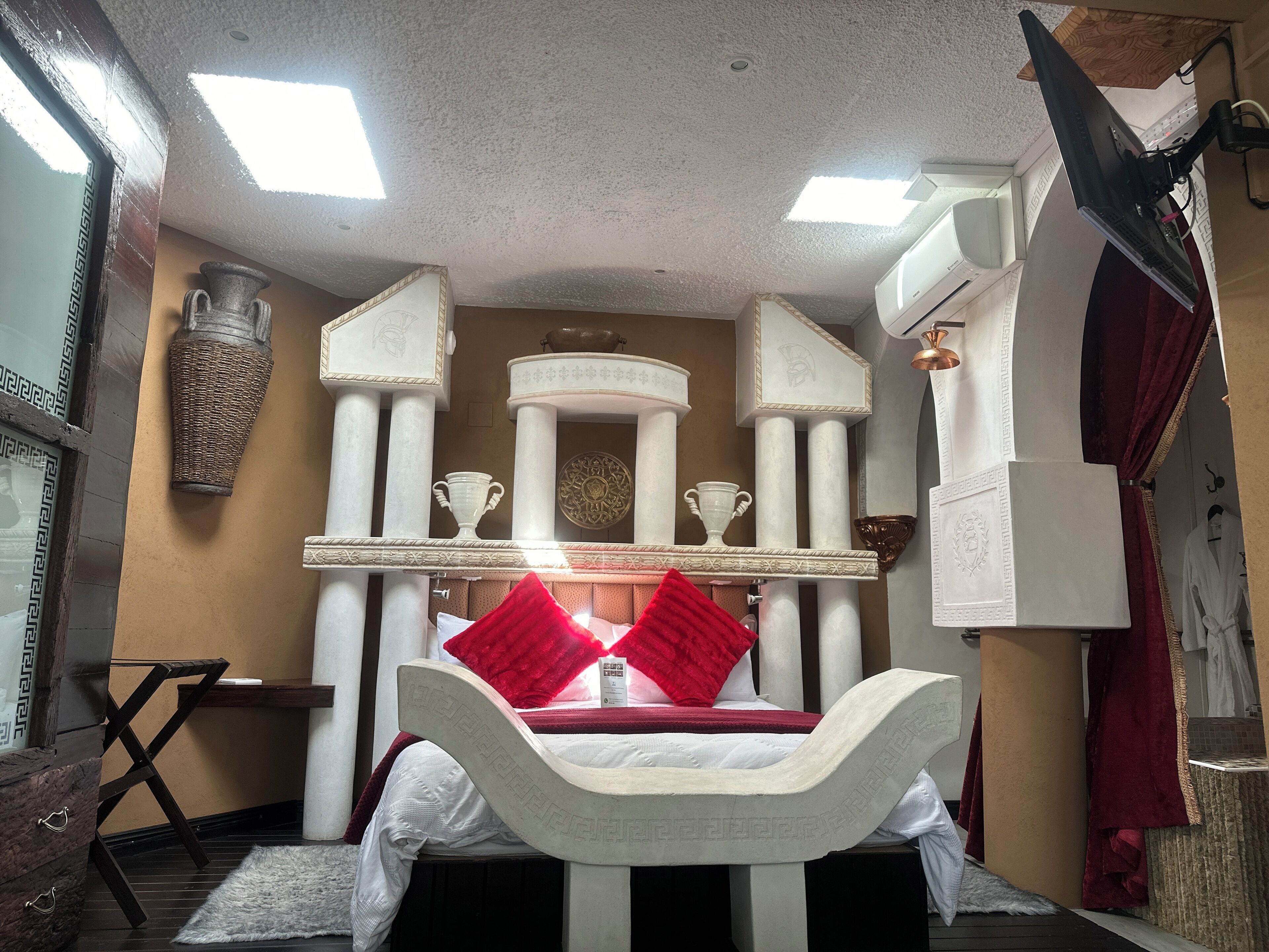 Une pièce comprenant un lit, un bureau, une chaise, un grand vase et un miroir.