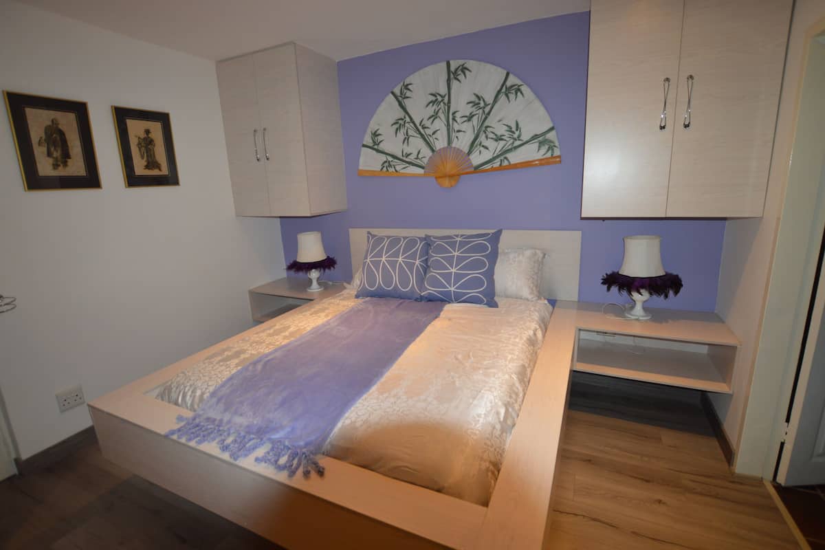 Un dormitorio con cama, mesitas de noche, un ventilador y un armario.