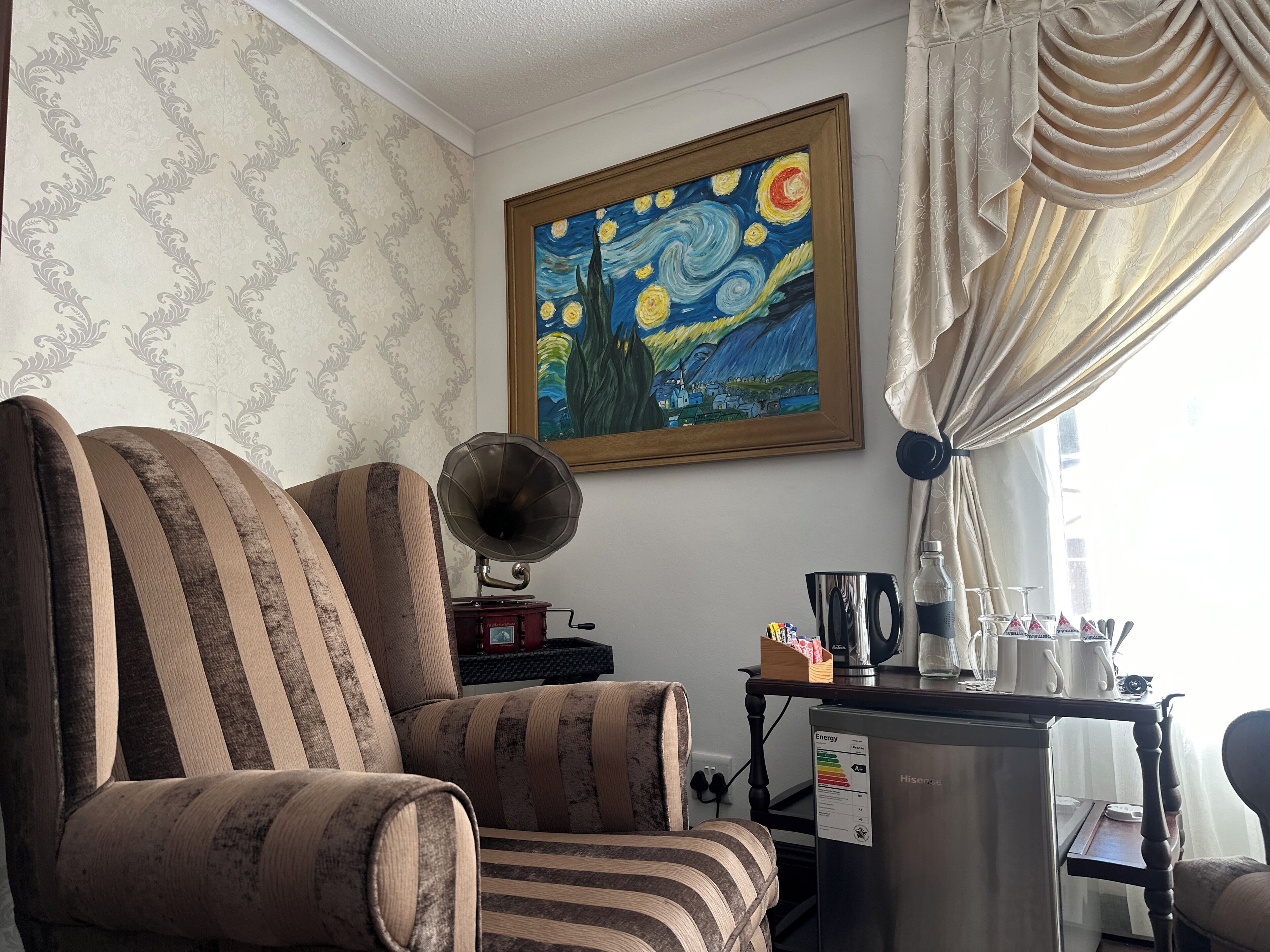 A room with a striped armchair, a gramophone, a painting of a night scene, and a table with a kettle and cups.