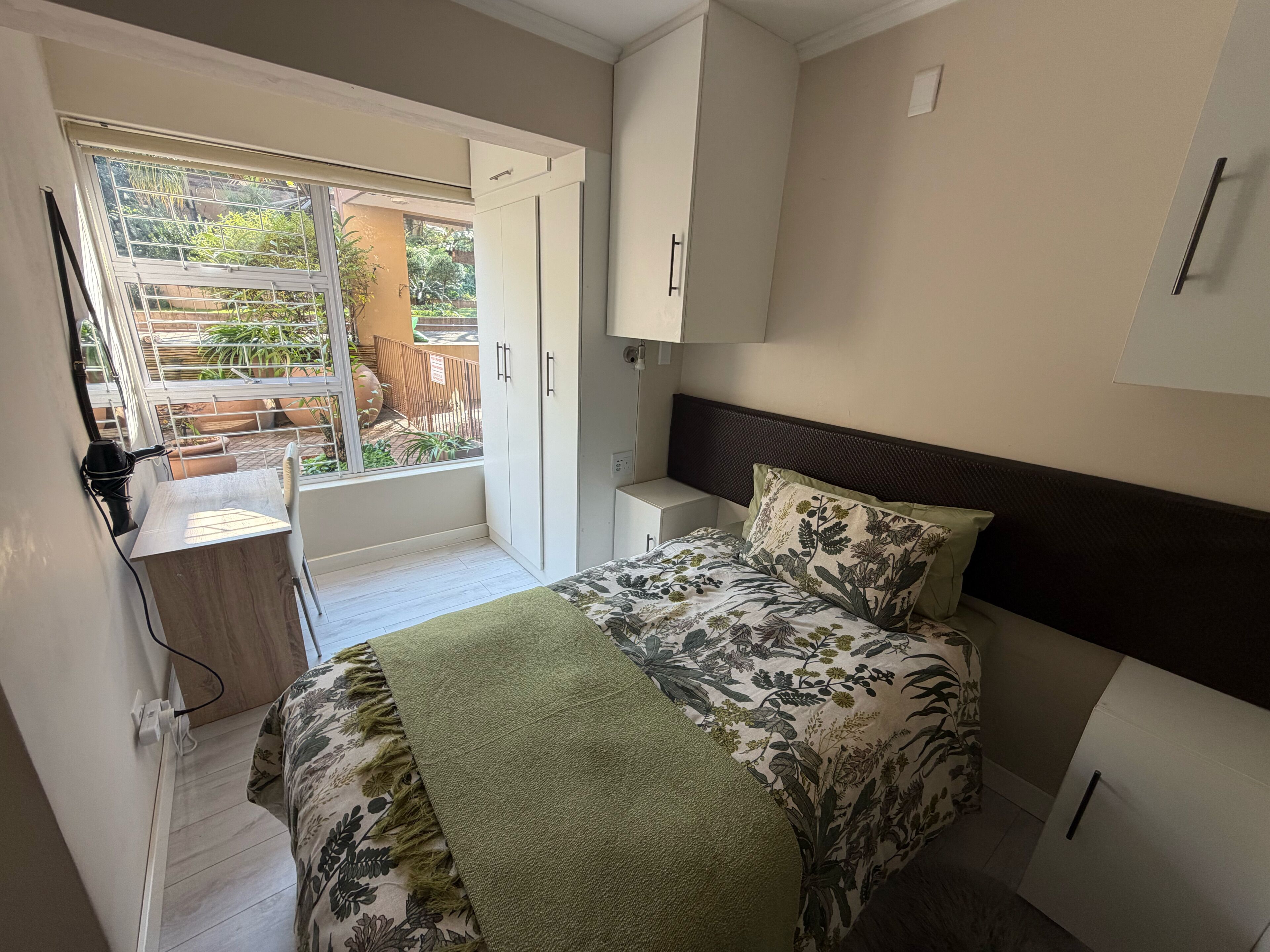 Un dormitorio con cama, escritorio y vistas al exterior.