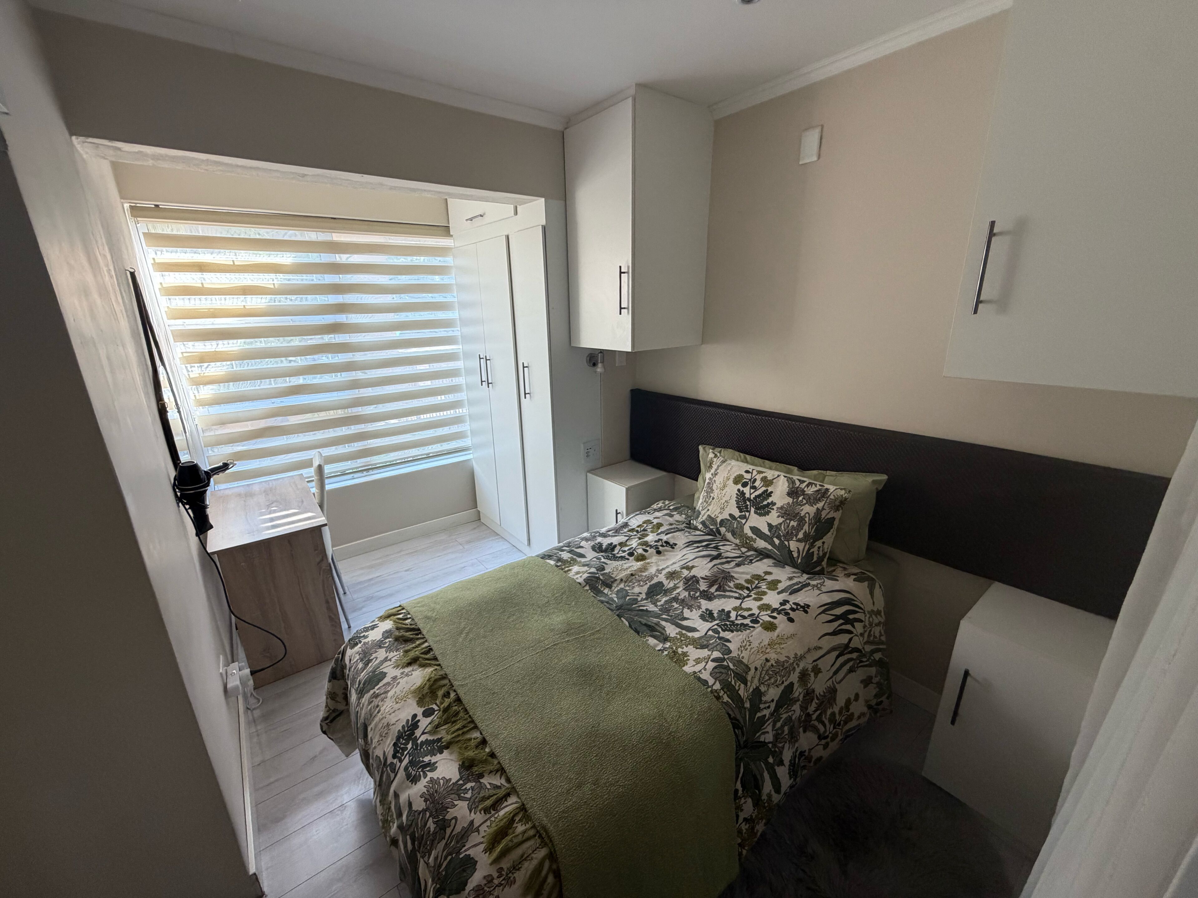 A bedroom with a bed, a desk, a wardrobe, and a window with blinds.