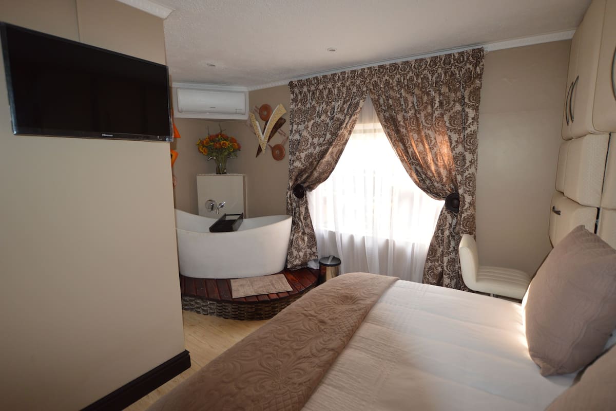 Habitación de hotel con una cama grande, una zona de estar con una silla, una bañera y un televisor montado en la pared.